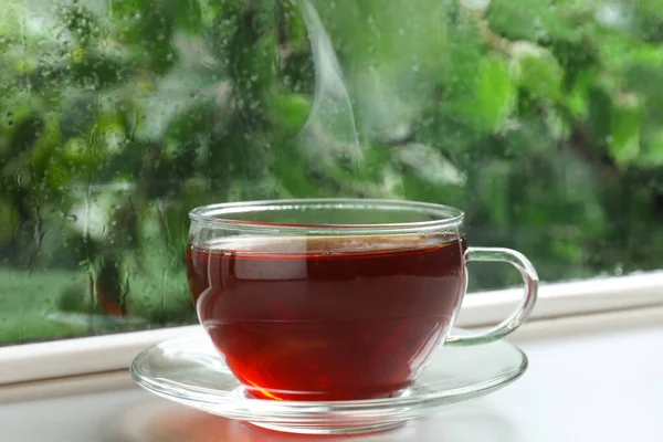 Glass cup of hot tea on windowsill. Rainy weather — Stock Photo, Image