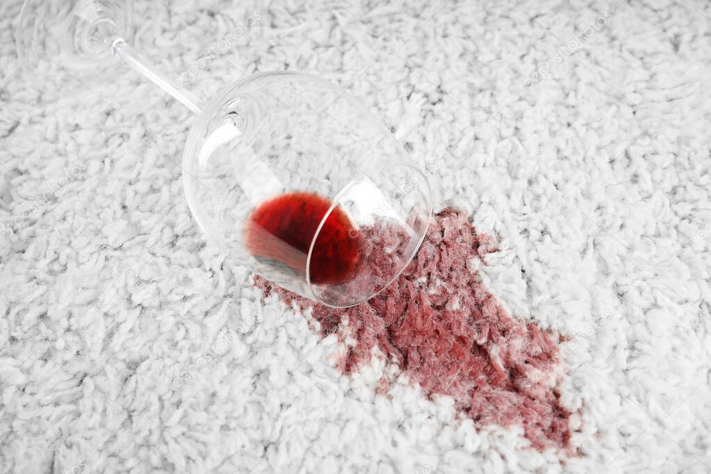 Overturned glass and spilled exquisite red wine on soft carpet