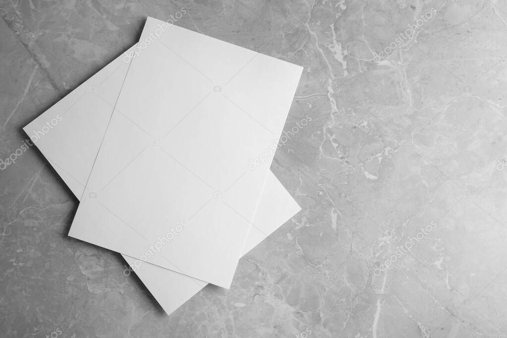 Blank paper sheets on light grey marble background, top view. Mock up for design