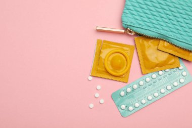 Prezervatifler ve çantada doğum kontrol hapları. Pembe arka planda. Üstü açık, mesaj için yer var. Güvenli seks.