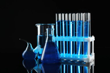 Siyah zemin üzerinde mavi sıvılar bulunan laboratuvar camları.