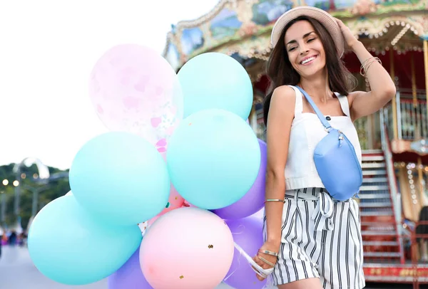 Attraktive junge Frau mit bunten Luftballons in der Nähe von Karussell — Stockfoto