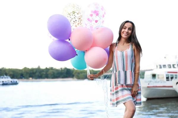 Hübsche junge Frau mit bunten Luftballons in der Nähe des Flusses — Stockfoto