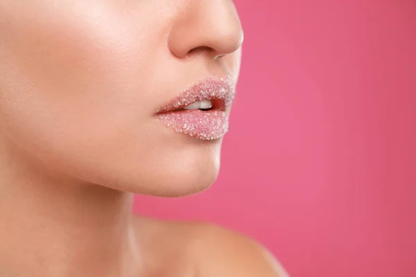 Young woman with sugar scrub on lips against pink background, closeup — ストック写真