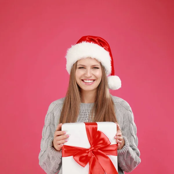 Joyeux jeune femme dans le chapeau de Père Noël avec cadeau de Noël sur fond rose — Photo