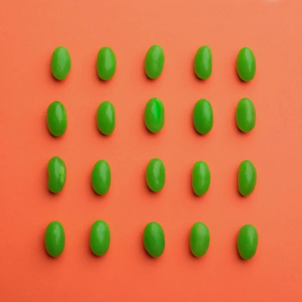 Green jelly beans on coral background, flat lay