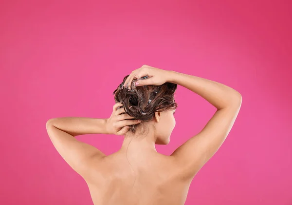 Giovane donna che lava i capelli su sfondo rosa — Foto Stock