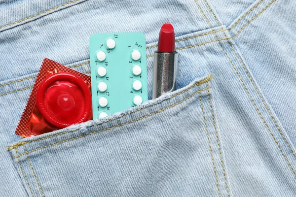 Vista da vicino di jeans con rossetto rosso e contraccettivi in tasca. Concetto sesso sicuro — Foto Stock