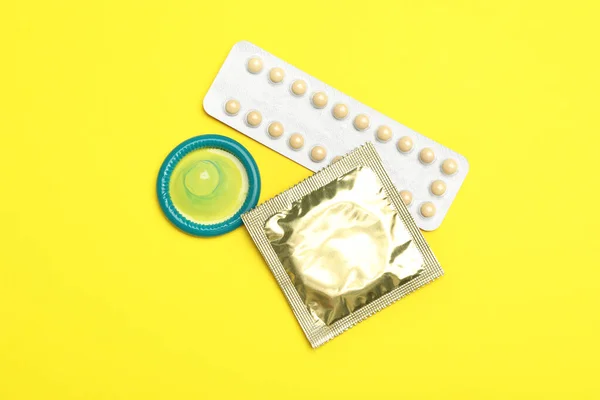 Préservatifs et pilules contraceptives sur fond jaune, à plat. Concept de sexe sûr — Photo