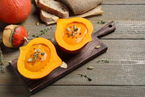 Tasty cream soup in pumpkin halves on wooden table — ストック写真