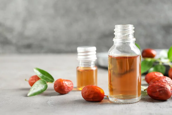 Bouteille en verre avec huile de jojoba et graines sur table en pierre grise. Espace pour le texte — Photo