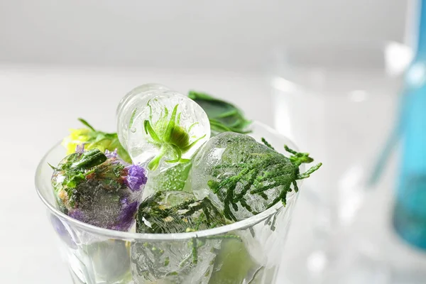 Glass of ice cubes with flowers on blurred background, closeup — ストック写真