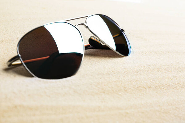Stylish sunglasses on white sand, space for text. Summer time