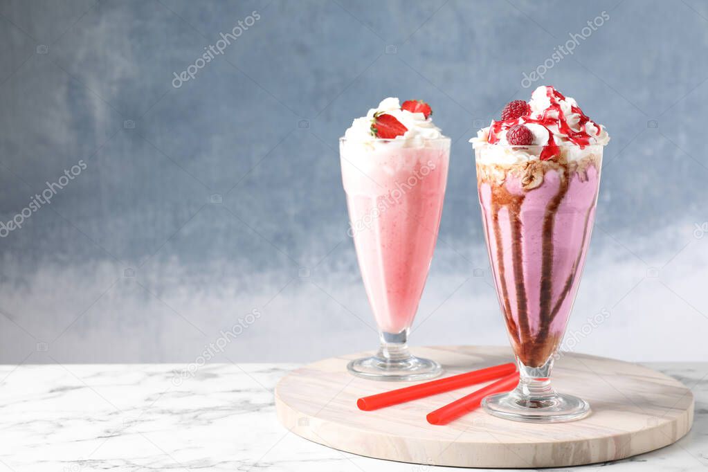 Tasty milk shakes with toppings on white marble table against blue background. Space for text