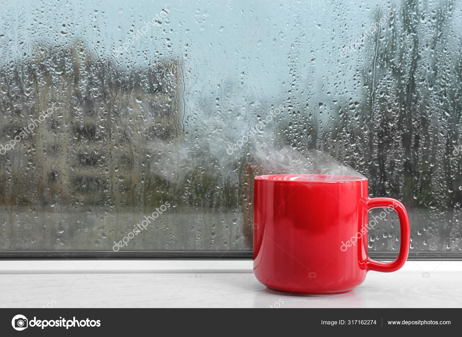 Cup of hot drink on windowsill, space for text. Rainy weather ...