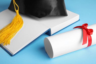 Mezuniyet şapkası, açık kitap ve açık mavi arka plan öğrenci diploması, yakın plan.