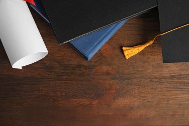 Mezuniyet şapkası ve öğrenci diplomasıyla ahşap masa üzerinde düz kompozisyon, metin için boşluk