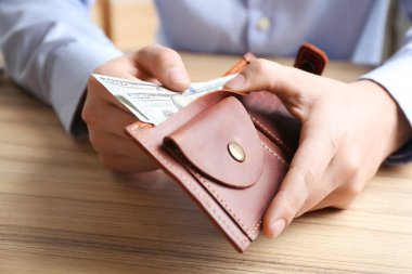 Ahşap masadaki cüzdana dolar banknotları koyan adam, yakın plan. Para tasarrufu