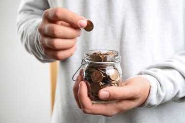 Kapalı mekandaki cam kavanoza bozuk para koyan adam, yakın plan. Para tasarrufu