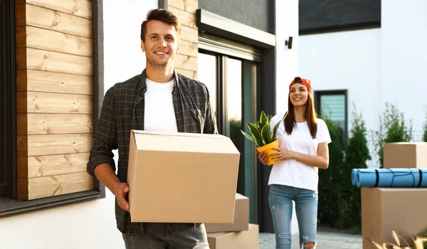 Happy couple with moving boxes and household stuff near their new house on sunny day