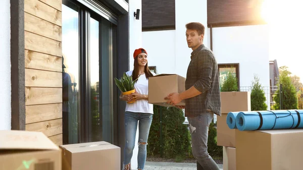 Pareja feliz con cajas móviles y cosas del hogar cerca de su nueva casa en el día soleado — Foto de Stock