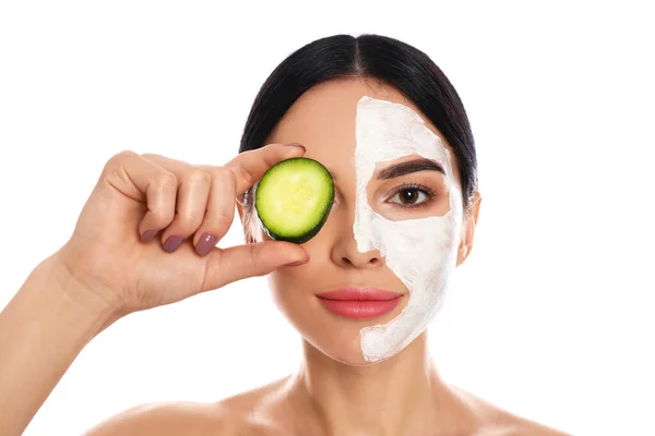 Young woman with cleansing mask applied on half of face holding cucumber against white background — Stock Photo, Image