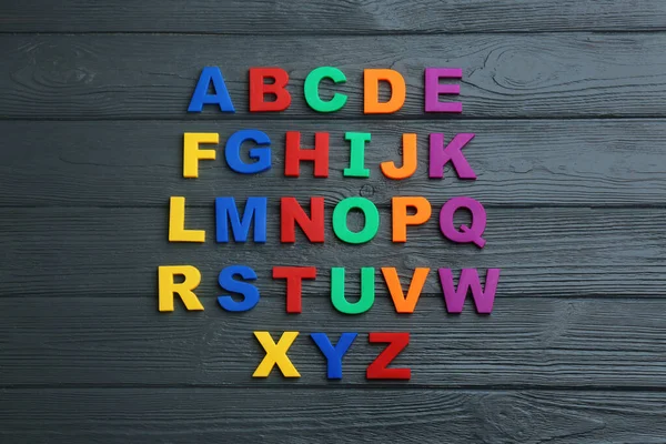 Lettere magnetiche colorate su sfondo nero in legno, posa piatta. Ordine alfabetico — Foto Stock
