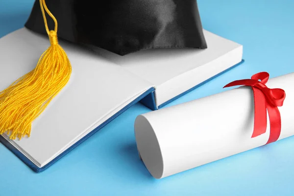 Cappello di laurea, libro aperto e diploma di studente su sfondo azzurro, primo piano — Foto Stock