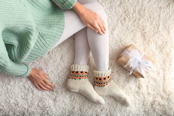 Woman wearing knitted socks on rug, top view. Warm clothes