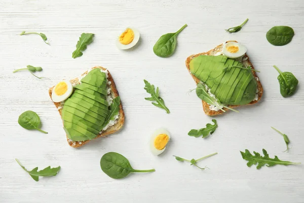 Flat lay composition with avocado toasts on white wooden table