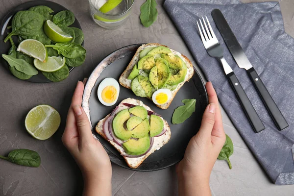 Vrouw met lekkere avocado toastjes over grijze tafel, bovenaanzicht — Stockfoto