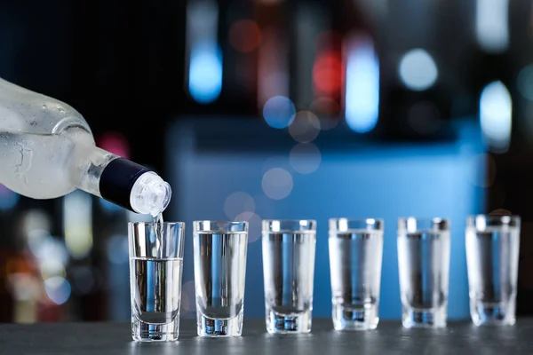 Pouring vodka from bottle into shot glasses on bar counter — Stock fotografie