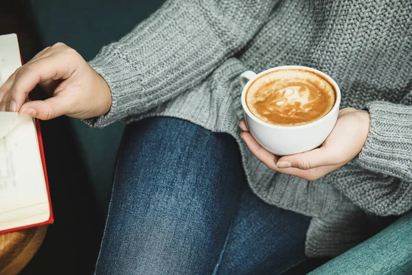 Woman with cup of coffee reading book at home, closeup — Stock Photo, Image