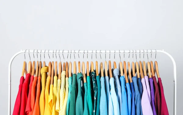 Rack met heldere kleren op lichtblauwe achtergrond. Regenboog kleuren — Stockfoto