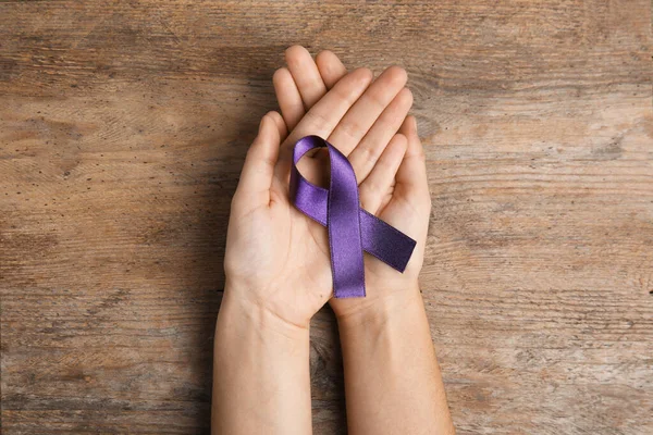 Mujer sosteniendo cinta púrpura sobre fondo de madera, vista superior. Sensibilización sobre violencia doméstica — Foto de Stock