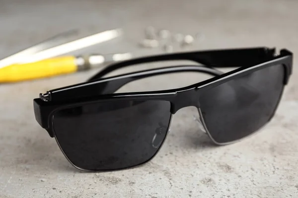 Óculos de sol elegantes e ferramentas de fixação na mesa cinza — Fotografia de Stock