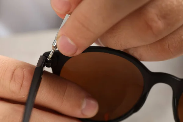 Handwerker repariert Sonnenbrille mit Schraubenzieher am grauen Tisch, Nahaufnahme — Stockfoto