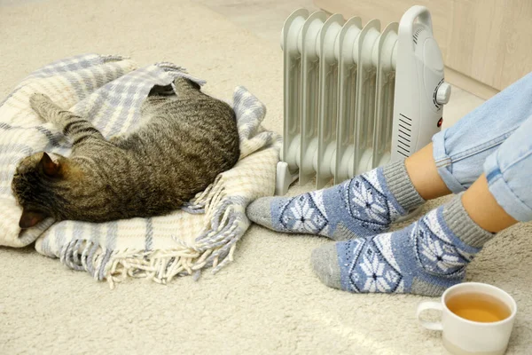 Jeune femme et mignon chat tabby près de chauffage électrique à la maison, gros plan — Photo