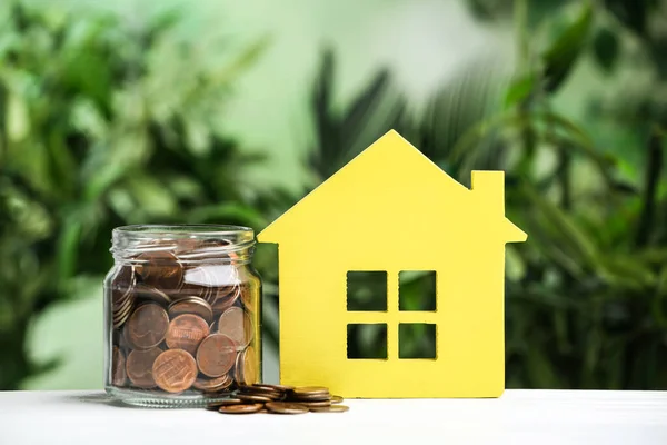 Modelo de casa amarilla y monedas sobre mesa de madera blanca sobre fondo borroso. Ahorro de dinero — Foto de Stock