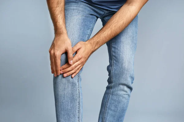 Чоловік, який страждає від болю в коліні на сірому фоні, крупним планом — стокове фото