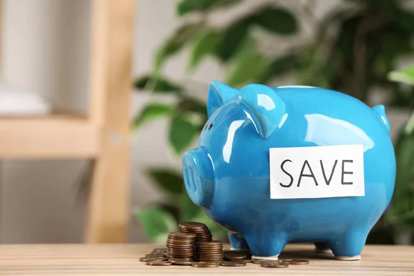 Piggy bank com palavra SAVE e moedas em mesa de madeira contra fundo desfocado — Fotografia de Stock