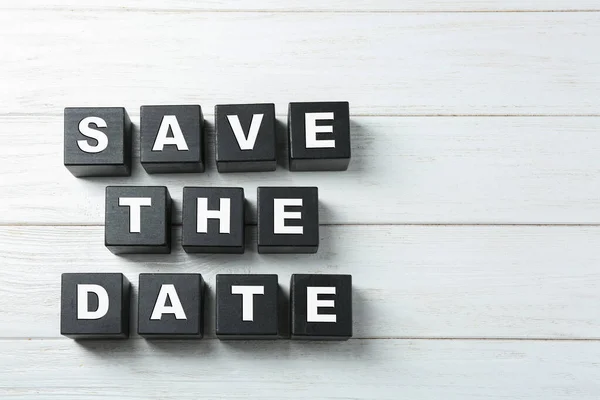 Επίπεδη σύνθεση με φράση Save The Date από μαύρους κύβους σε λευκό ξύλινο φόντο — Φωτογραφία Αρχείου