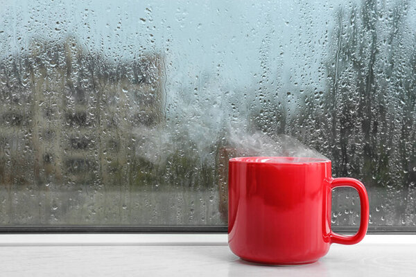 Cup of hot drink on windowsill, space for text. Rainy weather