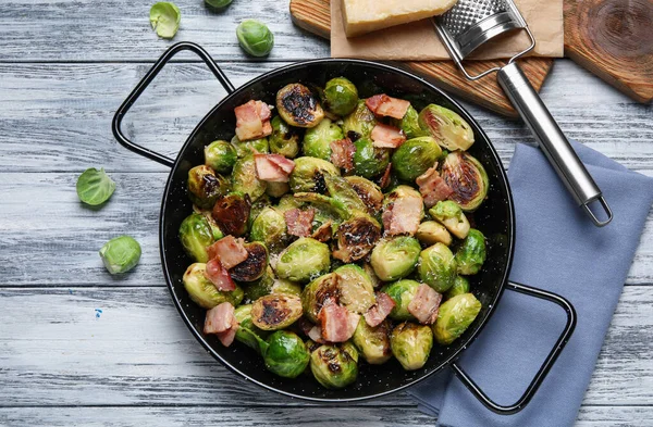 Deliciosos brotes de Bruselas con tocino en la sartén en la mesa de madera de color, la puesta plana — Foto de Stock