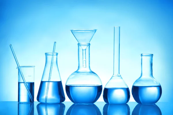 Лабораторное стекло с жидкими образцами для анализа на синем фоне — стоковое фото