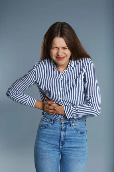 Femme souffrant de douleur dans le côté droit sur fond gris — Photo