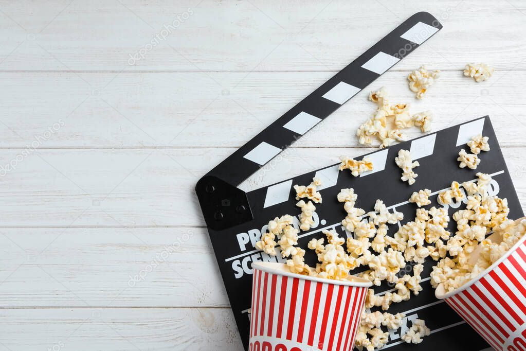 Clapperboard and popcorn on white wooden table, flat lay with space for text. Cinema snack