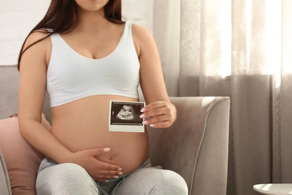 Pregnant woman with ultrasound picture at home, closeup. Space for text — Stock Photo, Image