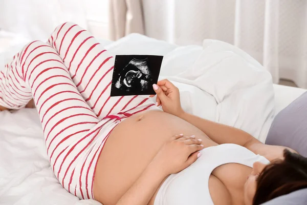 Pregnant woman with ultrasound picture on bed, closeup — Stock Photo, Image