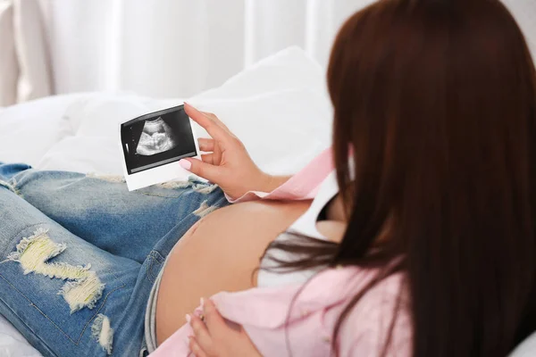 Pregnant woman with ultrasound picture on bed, closeup — Stock Photo, Image